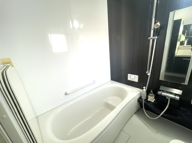 清潔感あふれるユニットバス。ゆったりとした浴槽で、一日の疲れをしっかり癒せます。手すり付きで安心感があり、ご家族皆様に配慮された設計。ダークカラーのアクセントパネルが空間を引き締め、上質な印象を演出。