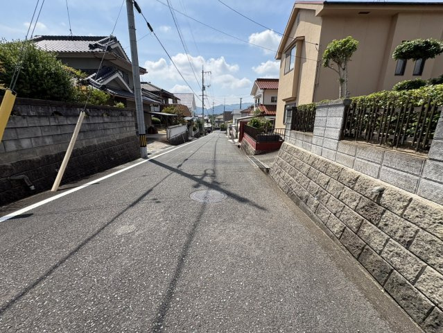 道路沿いには戸建住宅が建ち並び、穏やかな街並みが広がっています。前面道路は舗装されており、見通しも比較的確保されています。高台ならではの開放感があり、遠くには山並みも望める自然を身近に感じられる環境。