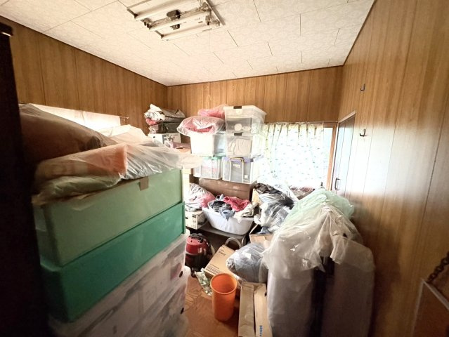 こちらの部屋は、木目調の壁に囲まれた落ち着いた空間で、現在は収納として利用されています。整理やリフォームを施せば、居室や書斎、趣味のスペースとしても活用可能です。窓からの採光もあり明るさを確保できます
