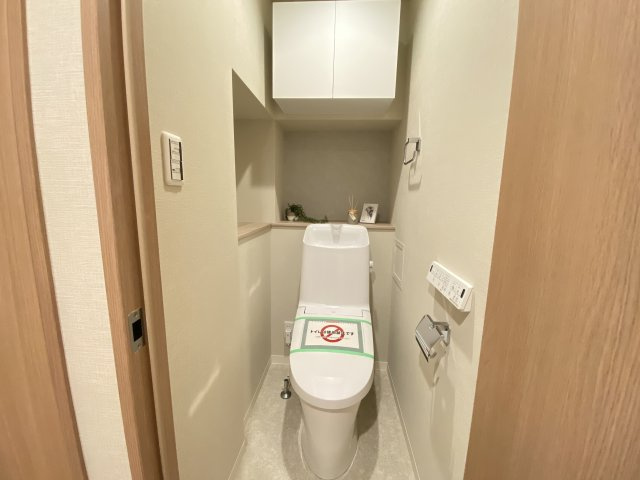 温水洗浄便座のトイレ設備です。奥行きの有るゆったりしたスペースには飾り棚や吊戸棚があり収納も便利です