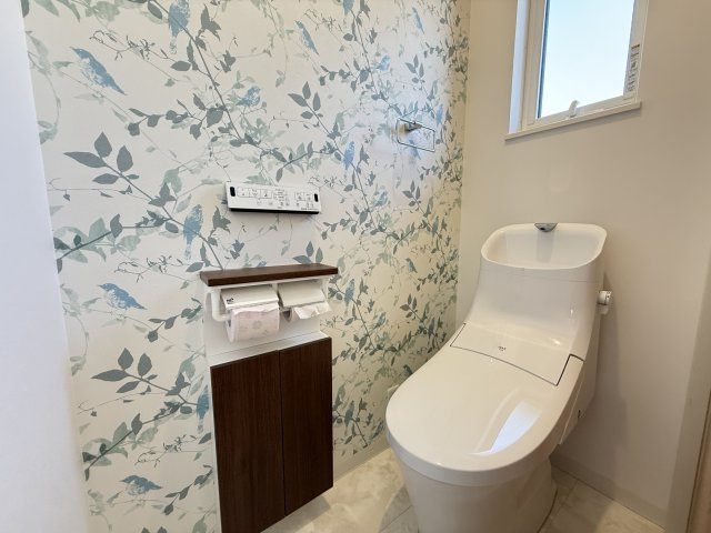 爽やかなデザインクロスを採用し、清潔感のある仕上がり。温水洗浄機能付きで快適に利用できます。収納付きの棚もあり、備品をすっきり保管可能。2階にもトイレがあることで、忙しい朝もスムーズに過ごせます。　　