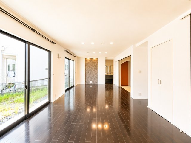 大きな掃き出し窓から陽光が差し込む開放的な空間です。ダイニングとリビングをゆったりレイアウトでき家族が自然と集まる心地よい住まいを演出。ダークカラーの床とアクセントウォールが上質な雰囲気引き立てます　