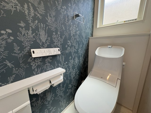 落ち着いたボタニカル柄のアクセントクロスが印象的なトイレ空間。温水洗浄便座を備え、毎日快適にご利用いただけます。窓付きのため換気もしやすく、明るさも確保。おしゃれで居心地の良い空間に仕上がっています。