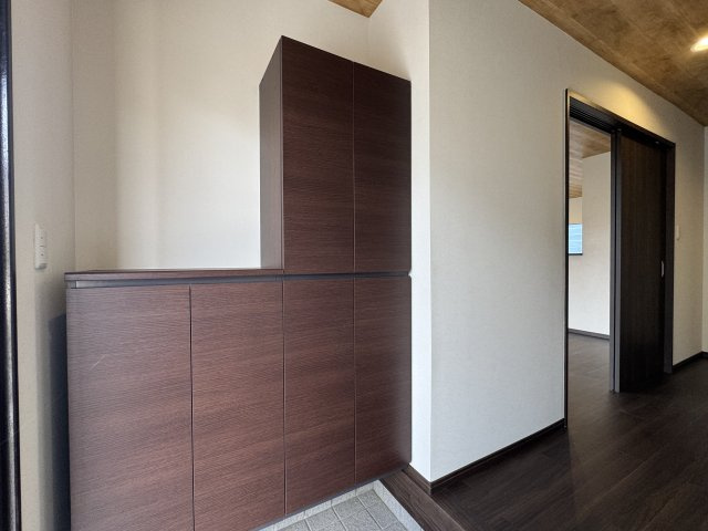 落ち着いた木目調のシューズボックスが印象的な玄関。　広々としたスペースで来客時もゆとりがあります。　収納力もあり、家族全員の靴をすっきり収納可能。　清潔感と高級感が調和した玄関空間です。