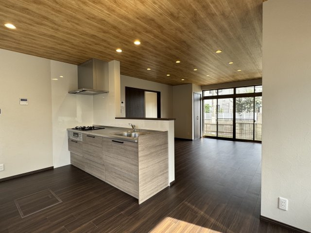 木目調の天井とフローリングが温かみを演出する18帖の広々LDK。　南面の大きな窓から明るい光が差し込み、開放感あふれる空間です。　対面式キッチンで家族の会話も弾み、心地よい時間を過ごせます。