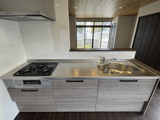 木目調の落ち着いたデザインが魅力のシステムキッチン。　広々としたシンクと作業スペースが確保されています。　家族との会話を楽しみながら料理ができる対面式で、開放感と温かみのある空間を演出しています。
