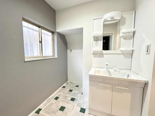 おしゃれなクッションフロアを敷いた洗面所です。クロスは一部色を変え、引き締まって落ち着いた雰囲気になっています。壁に洗濯機を置くスペースを収納している為、洗面所をすっきりと広く使うことができます。