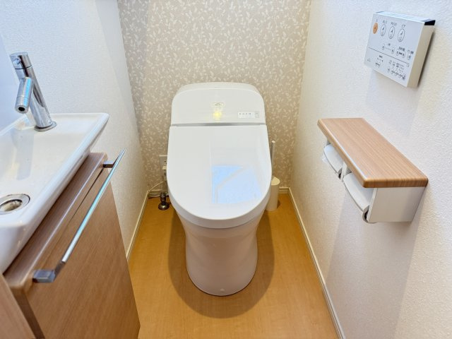 木目調の床とアクセントクロスが調和した温かみのあるトイレスペース。ウォシュレット機能付き便座で清潔かつ快適に利用できます。明るい採光が取り込める窓もあり換気面でも安心。細部まで配慮された快適性が魅力。