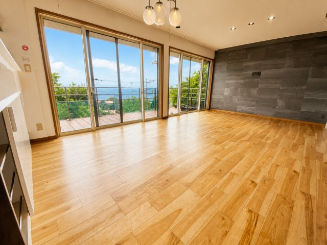 広々としたリビング、大きな窓から差し込む爽やかな日差しと風、暖かい色のフローリングが特徴です。