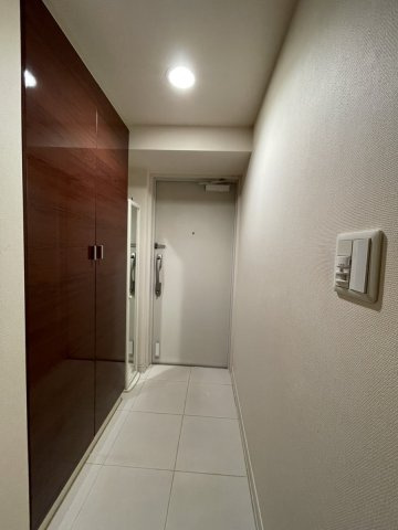 【玄関】光沢のある木目調の収納と白いタイル床が高級感を演出。落ち着いた雰囲気でゲストを迎えます。