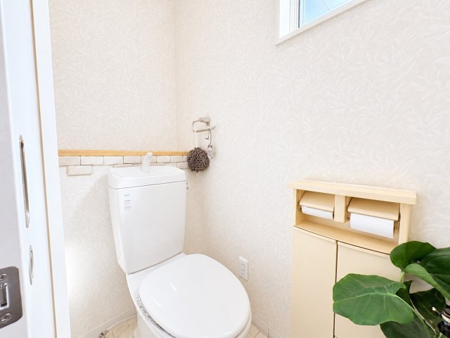 白を基調とした内装に、やわらかな色合いのアクセントが調和する落ち着いたトイレ空間です。窓が設けられているため、自然光を取り込みやすく、換気にも便利です。居心地の良さにも配慮された空間となっています。