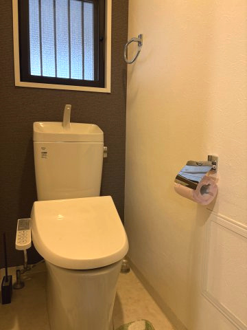 水回りに窓が設置され、心地よい風が通る明るいトイレ空間です。温水洗浄便座付きで日々の暮らしも快適。ブラウンのアクセントクロスが落ち着いた雰囲気を演出し、手洗いタンクも備わっています。