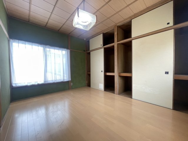 一面に大きな収納を備えた実用性の高い洋室。十分な収納があり、衣類や寝具、季節用品などをすっきりと片付けられます。床は明るいフローリング、壁は落ち着いた緑の壁で、和の風合いと現代的な住み心地を両立。