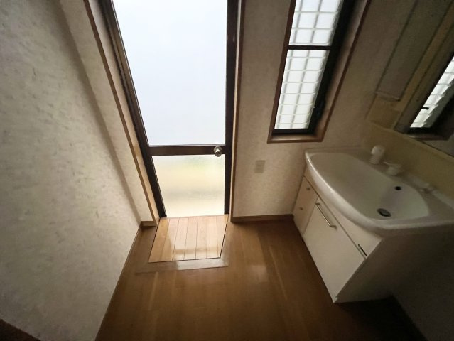 浴室に隣接した洗面・脱衣スペースです。洗面化粧台には大きな鏡と収納を備えており、洗面用品や日用品を整理しやすい造り。勝手口が設けられているため、換気やゴミ出し等の屋外への出入りも可能です。