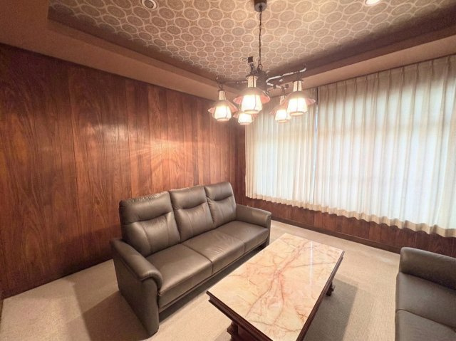 落ち着いた雰囲気の内装が印象的なリビングスペースです。壁面の木目調デザインが空間に温かみを与え、ゆったりとした時間を過ごせる居心地の良い空間となっています。大きな窓から自然光も入ります。