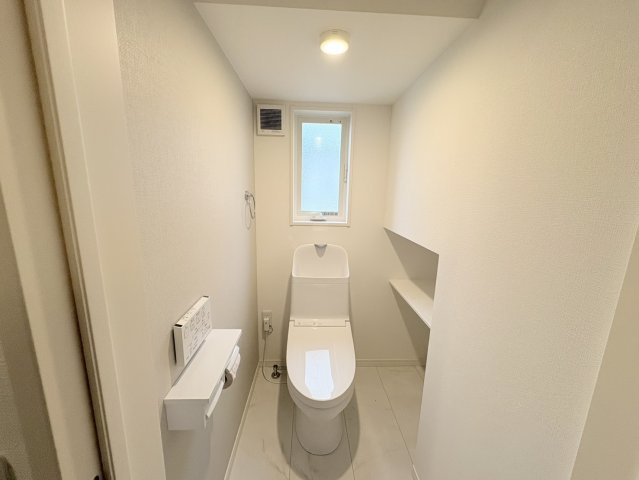 清潔感あふれるシンプルなトイレ空間。窓付きで自然光と換気が確保され、明るく快適にお使いいただけます。操作しやすい設備に加え、壁面にはちょっとした小物を置けるカウンターも設置されており実用性も良好。