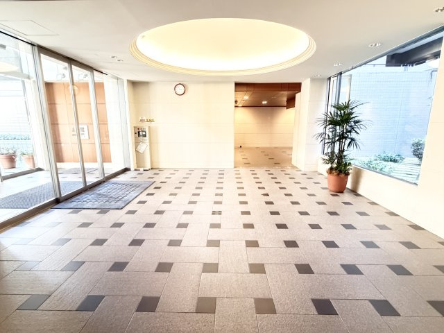 円形の折り上げ天井とやわらかな照明が優しく迎えるエントランス。大きなガラス窓から自然光と緑が差し込み、明るく清潔感あふれる開放的な空間です。