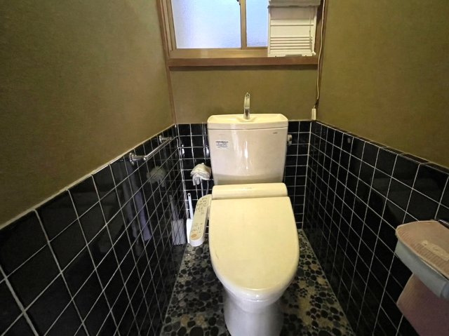 落ち着いたタイル張りのトイレ空間。温水洗浄便座付きで快適に使用できます。窓があり自然換気ができるため清潔に保ちやすいのもポイント。手すりも設置されており、安心して利用できる配慮された造りです。