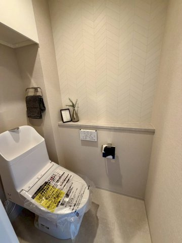 温水洗浄便座完備の洋式トイレ。手元で操作できる壁面リモコンで快適な使い心地。　扉付きの吊り戸棚も付いています。