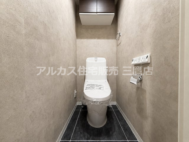 ニュアンスカラーのクロスとシックな床タイルのコントラストが美しい洗面所・トイレ空間。上部には便利な吊戸棚収納が備わっています。