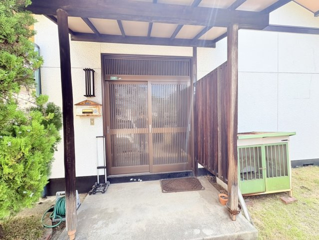 屋根付きの玄関ポーチで、雨の日にも玄関前で傘を開閉しやすい造り。木の柱や格子状の玄関扉が和風住宅らしい趣を演出し、植栽の緑と調和した落ち着きのある外観。住まいのプライベート感にも配慮された玄関まわり。