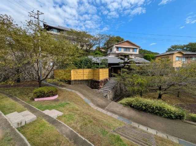 豊かな緑に囲まれた高台に佇む、趣のある和の住まい。道路から建物までゆとりがあり、石積みや竹垣、庭木が周囲の景観と美しく調和しています。開放的な景色も印象的で、落ち着いた住環境を感じられます。