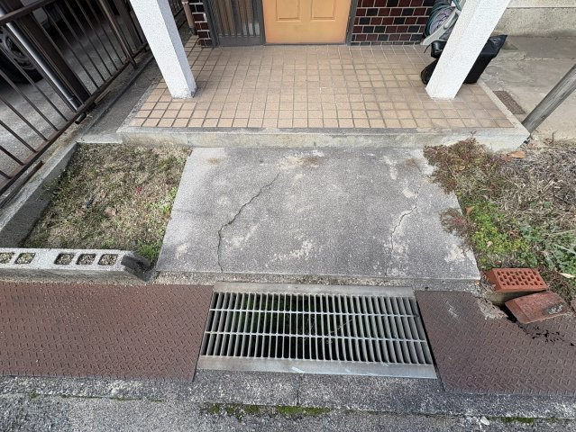 玄関前はタイル敷きのアプローチとなっており、安定感のある造りで出入りもスムーズ。道路との高低差も比較的緩やかで日常の動線に配慮されています。雨水排水用の側溝も整備されており、実用性を重視した外構です。