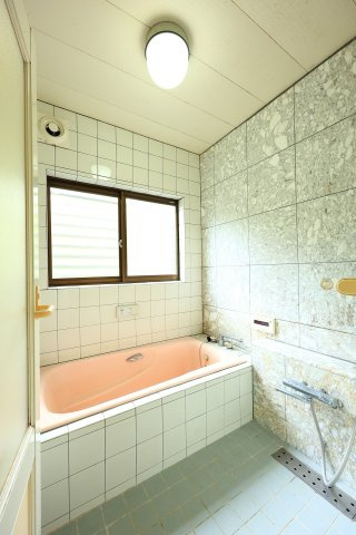 壁面の高級感ある大理石調タイルと、優しいピンク色の浴槽が印象的なバスルーム。大きな窓があり、外の自然を感じながら換気もスムーズに行えます。毎日の疲れをゆったりと癒やせる広さです。